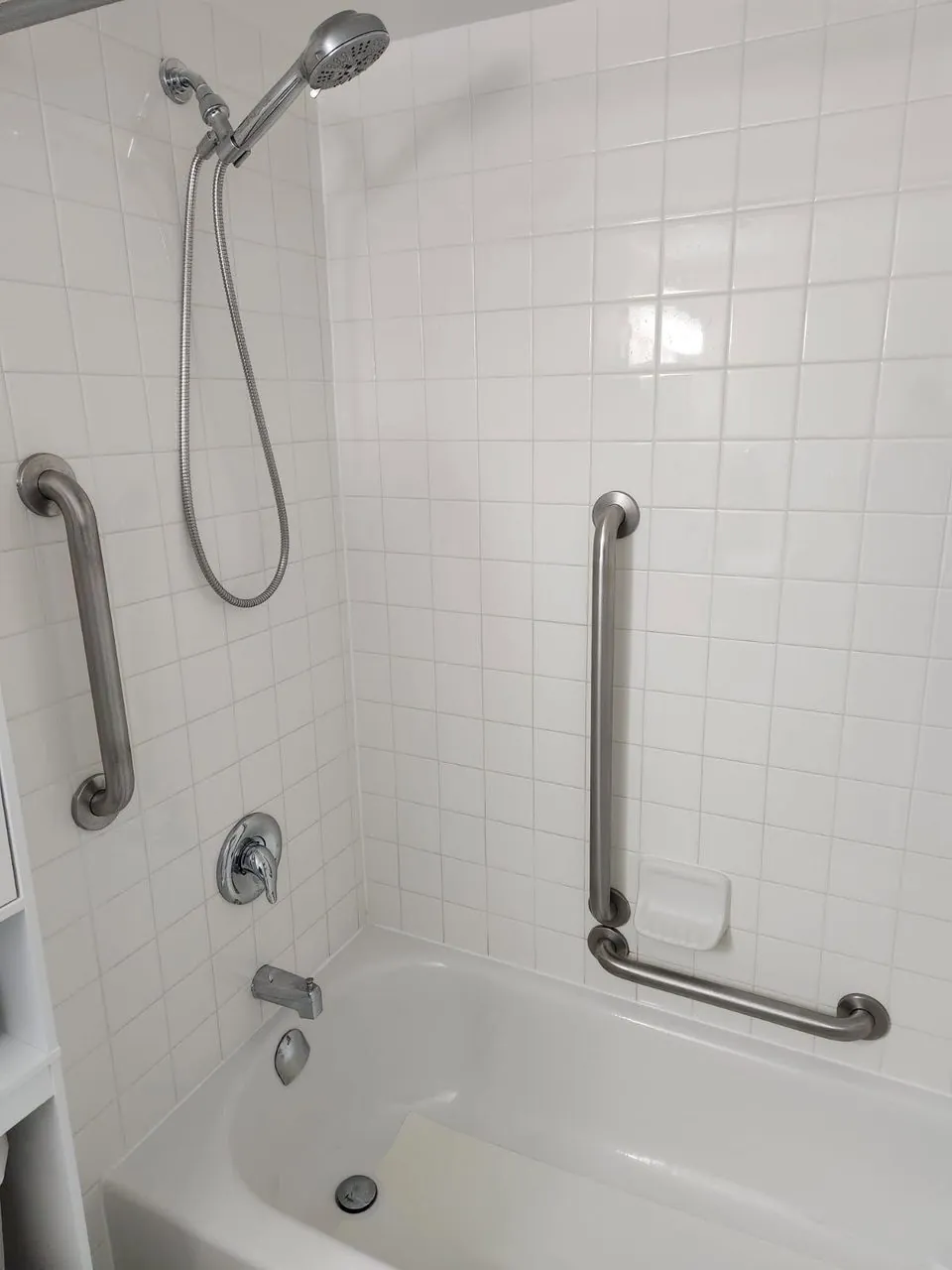 Stainless grab bars and a handheld shower fitted in a white-tiled tub, ready for a safe return home
